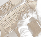 Person typing at a computer keyboard with a notepad and video footage visible on the monitor.